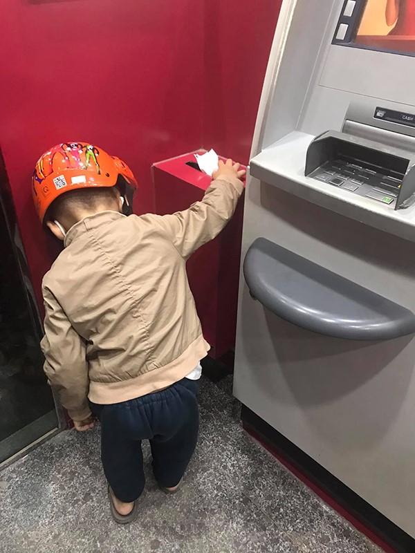 Cậu bé cúi xuống nhặt rác bỏ vào thùng ở cây ATM.